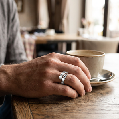 Jeden srebrny pierścionek LOVE i krzyż na dłoni przy kawie w restauracji